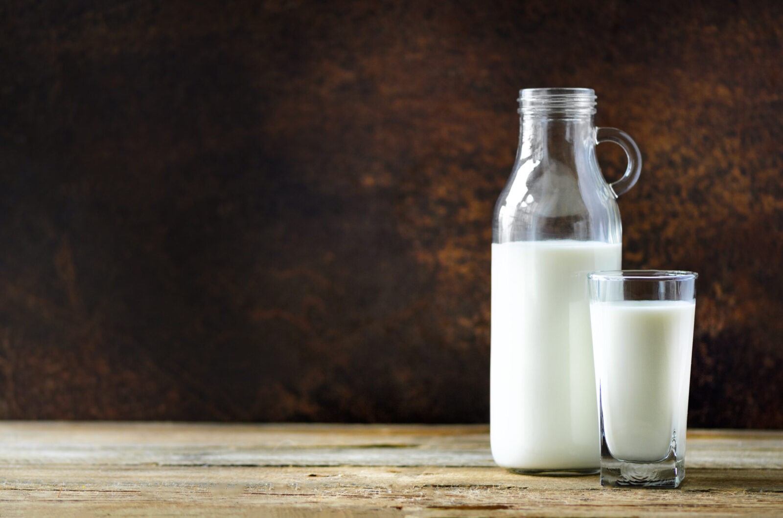Milk bottle and glass on wooden table, dark background. Healthy eating concept. Copy space